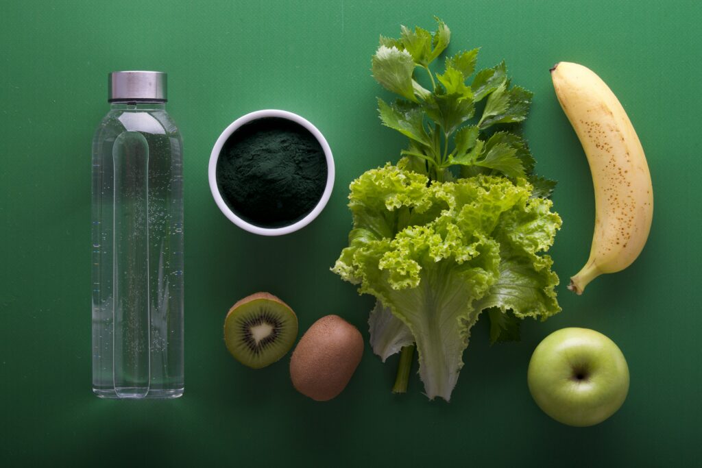 A flat-lay image of fresh fruits, vegetables, and a bottle of water. 